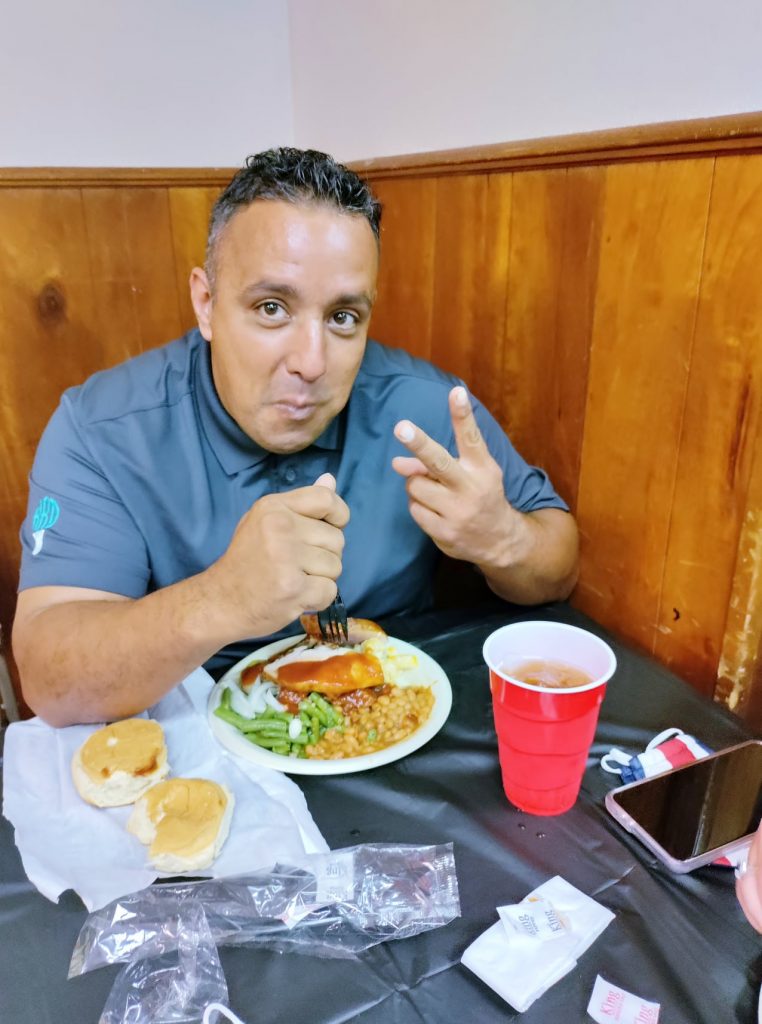 A man with short dark hair sits at a table preparing to enjoy the luch sitting in front of him.